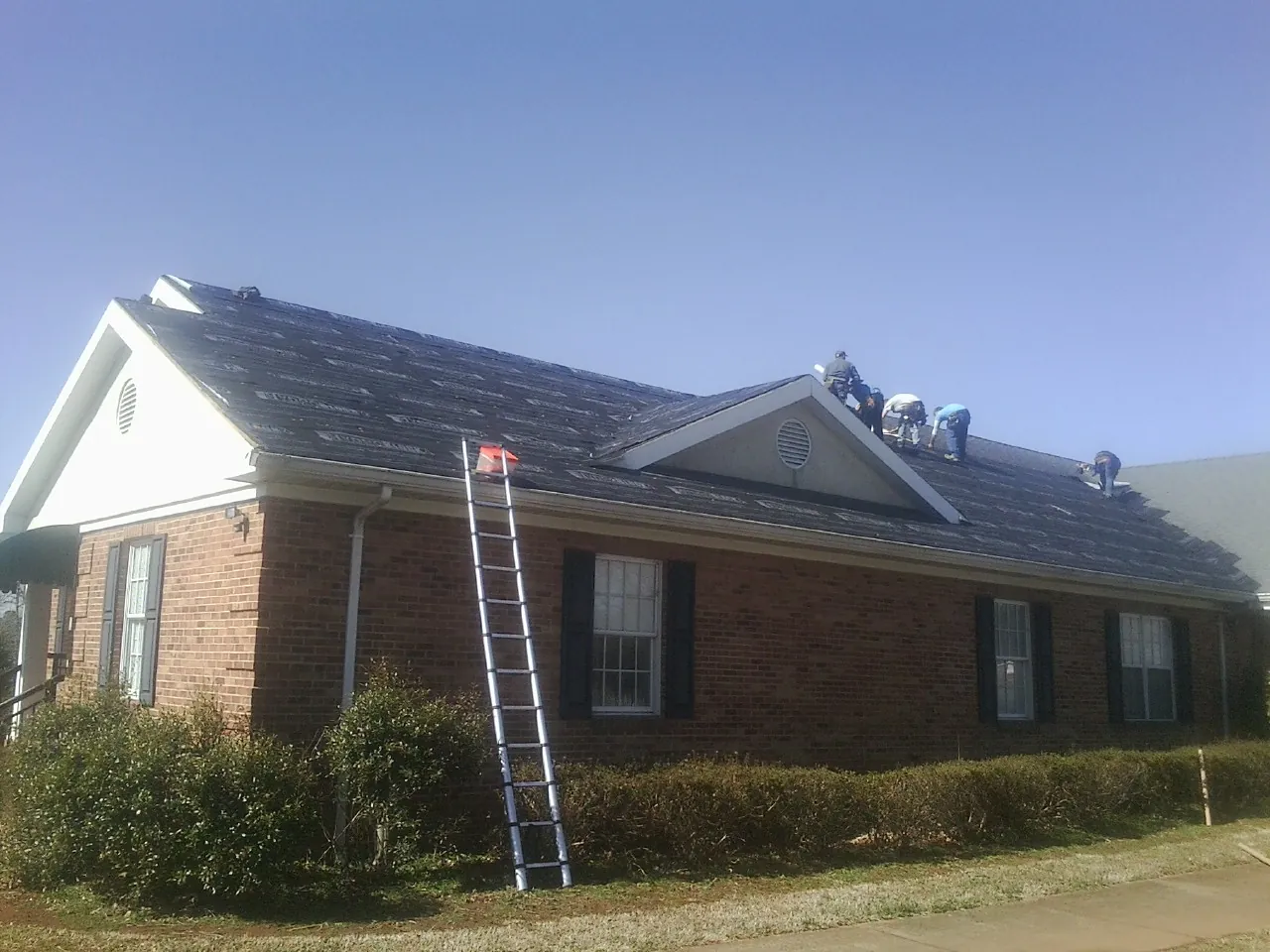 Crew tearing shingles off a brick ranch roof with a ladder set — Emergency Roof Repair work by our crew in Eaton