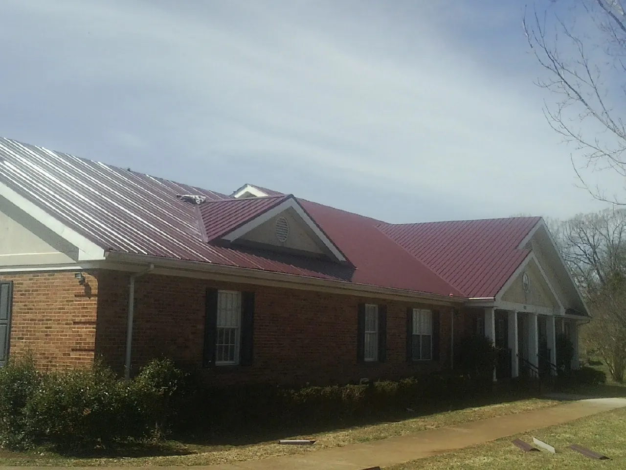 Red metal roof with gabled entries on a long brick building, from a Hail Damage Roof Repair job in Eaton