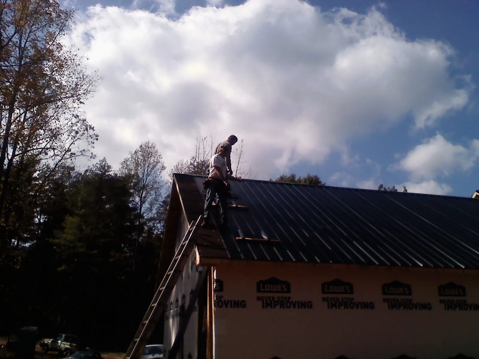 Roofer fastening dark metal panels high against a cloudy sky, from a Roof Inspection job in Eaton